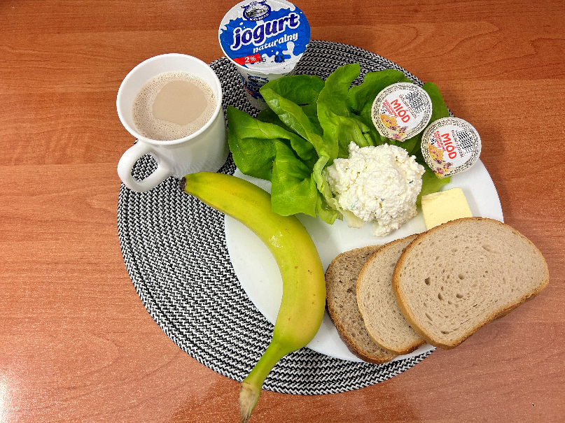 Na zdjęciu znajduje się: Jogurt naturalny, Kawa zbożowa z mlekiem, Chleb mieszany pszenno-żytni, Chleb Graham, Masło extra 82%, Twarożek, Miód, Banan, Sałata zielona